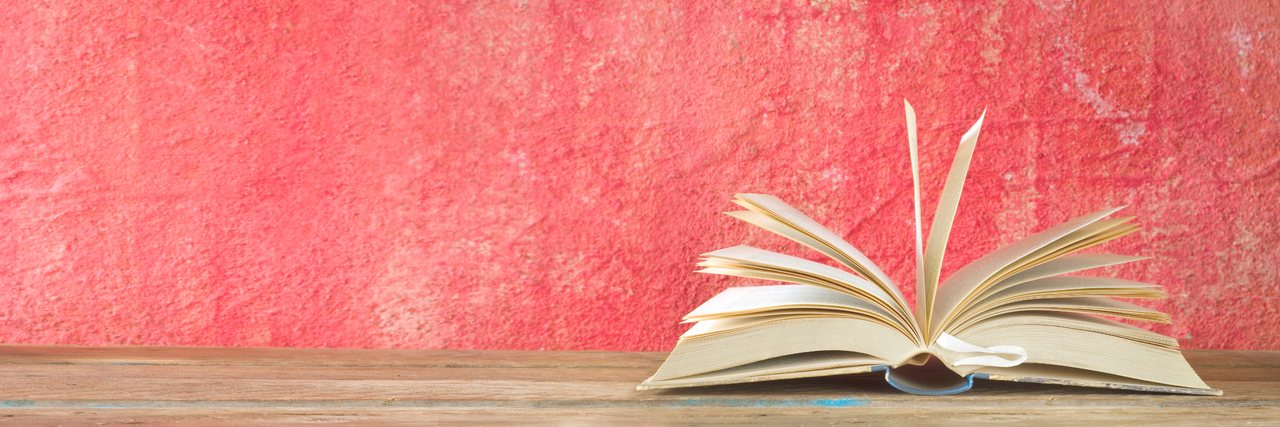 Ein Buch liegt aufgeschlagen auf einem Tisch vor einer rosa Wand