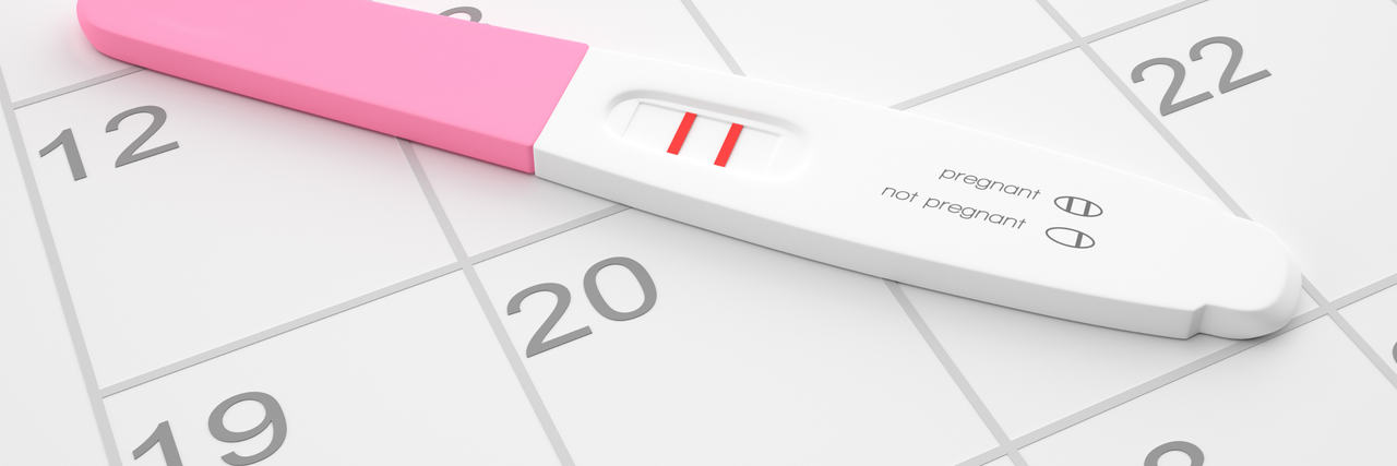 Ein weiß-pinker, positiver Schwangerschaftstest liegt auf einem Kalenderblatt