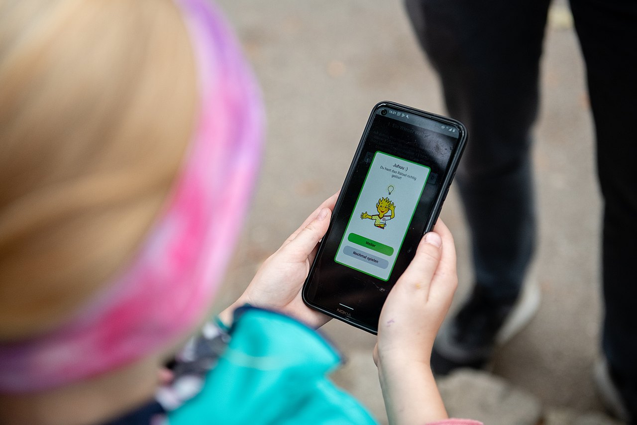 Kinderaktiv-App Kind schaut unterwegs auf einem Smartphone in die Kinderaktiv App