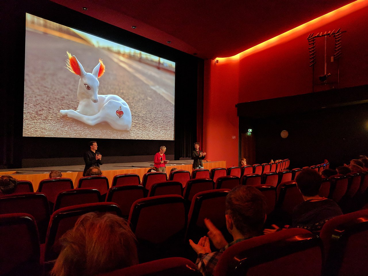 Innenansicht eines dunklen Kinosaals während einer Vorführung, mit leeren roten Sitzreihen im Vordergrund.