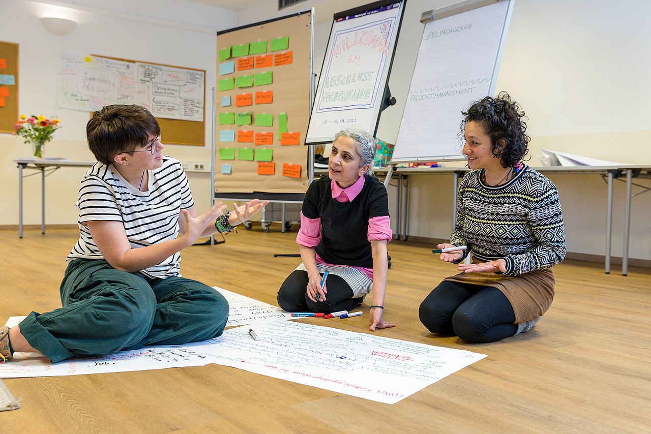 Angeregte Diskussion Drei Personen, die am Boden sitzen und angeregt diskutieren