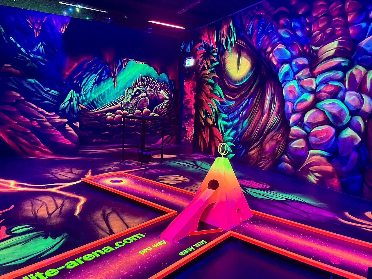Minigolfbahn in einem dunklen Raum, an der Wand dahinter sieht man einen Drachen