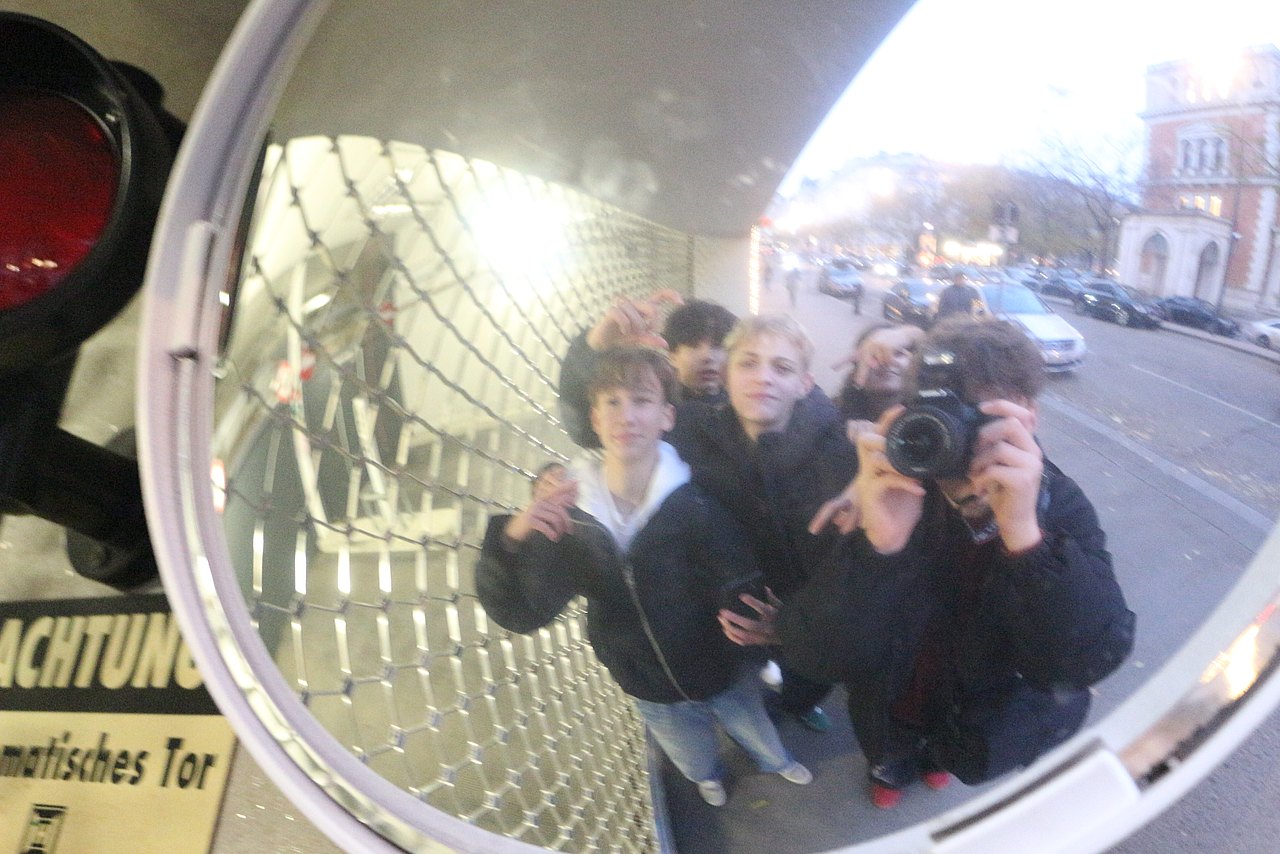 Fotowalk von und mit Jugendlichen Ein Jugendlicher fotografiert einen runden Straßenspiegel, in der Reflexion sieht man ihn und seine Freunde.