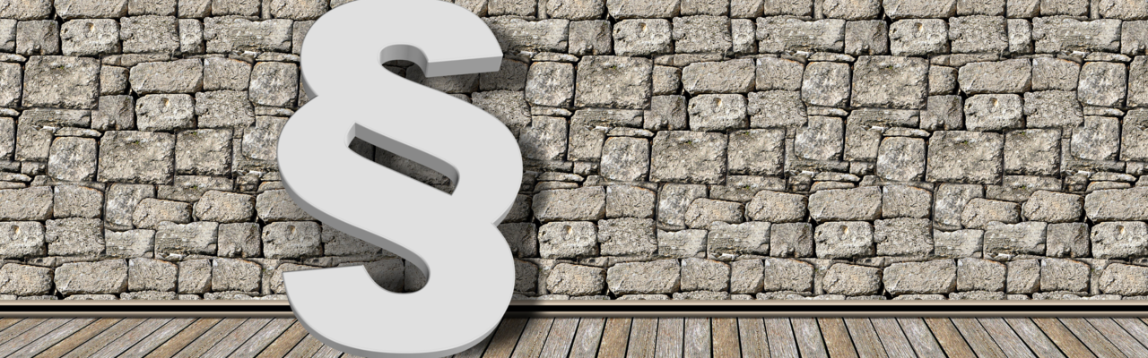 Ein Paragrad Symbol steht angelehnt an eine Mauer