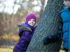 Maedchen im Anorak lehnt an einem Baum