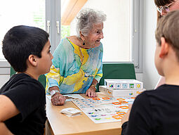 EAW Schüler spielen mit Seniorin ein Brettspiel.