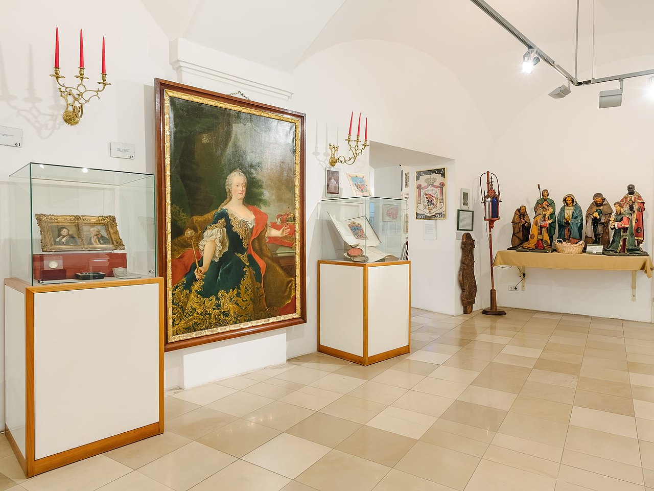 Ausstellungsraum im Bezirksmuseum der Innenstadt mit Gemälden, Schaukästen und Krippenfiguren.