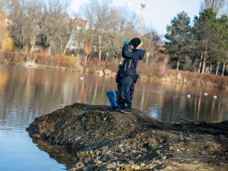 Zwei Kinder blicken mit ihren Fernglaesern über einen herbstlichen Donau-Altarm.