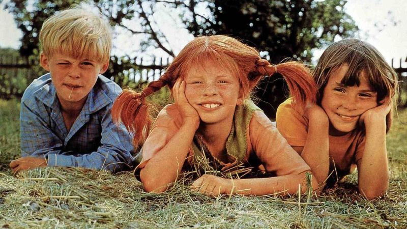 Pippi Langstrumpf liegt mit ihren Freunden Annika und Tommi auf der Wiese.