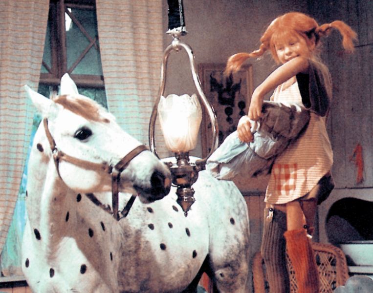 Pippi Langstrum steht auf einem Tisch neben ihrem Pferd Kleiner Onkel. 