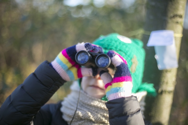 Wanderholli Badges Mädchen schaut durch Fernglas beim Winterwandern in Wien.