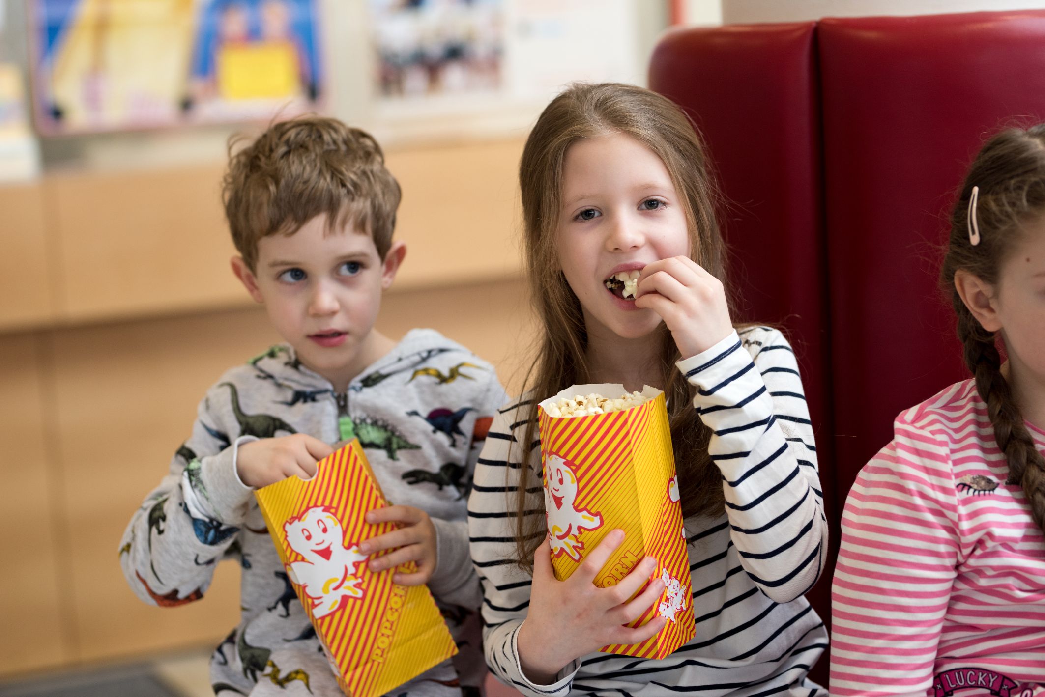 Ein Bub und ein Mädchen in gestreiften Shirts sitzen im Kinofoyer und essen Popcorn..