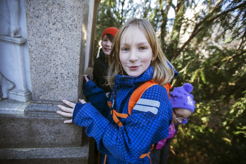 Ein Mädchen mit blauer Jacke schaut hinters Denkmal.