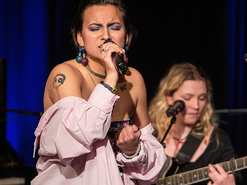 Ein Sängerin im Vordergrund und eine Gitarristin im Hintergrund.