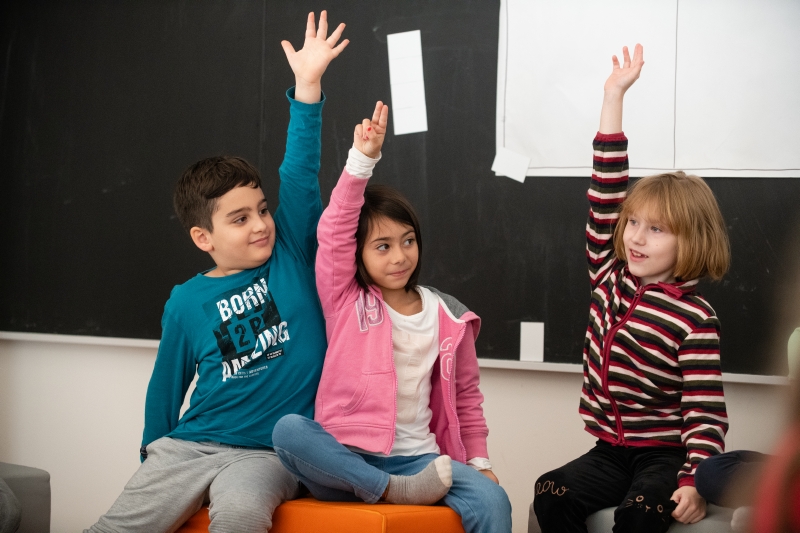 Drei Kinder wissen die Antwort und zeigen auf.