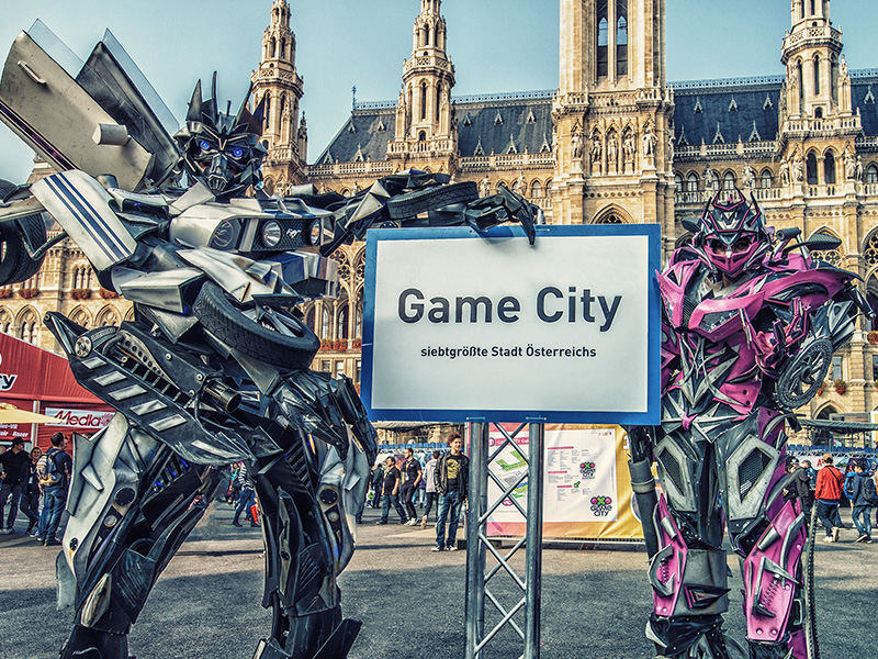 Game City Überdimensionale Actionfiguren stehen vor dem Rathaus und halten ein Game City Ortsschild in die Höhe