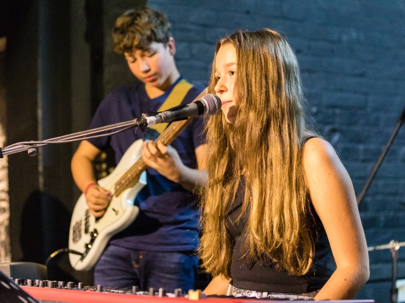 Eine junge Sängerin sitzt vor dem Keyboard und singt ins Mikrofon. 