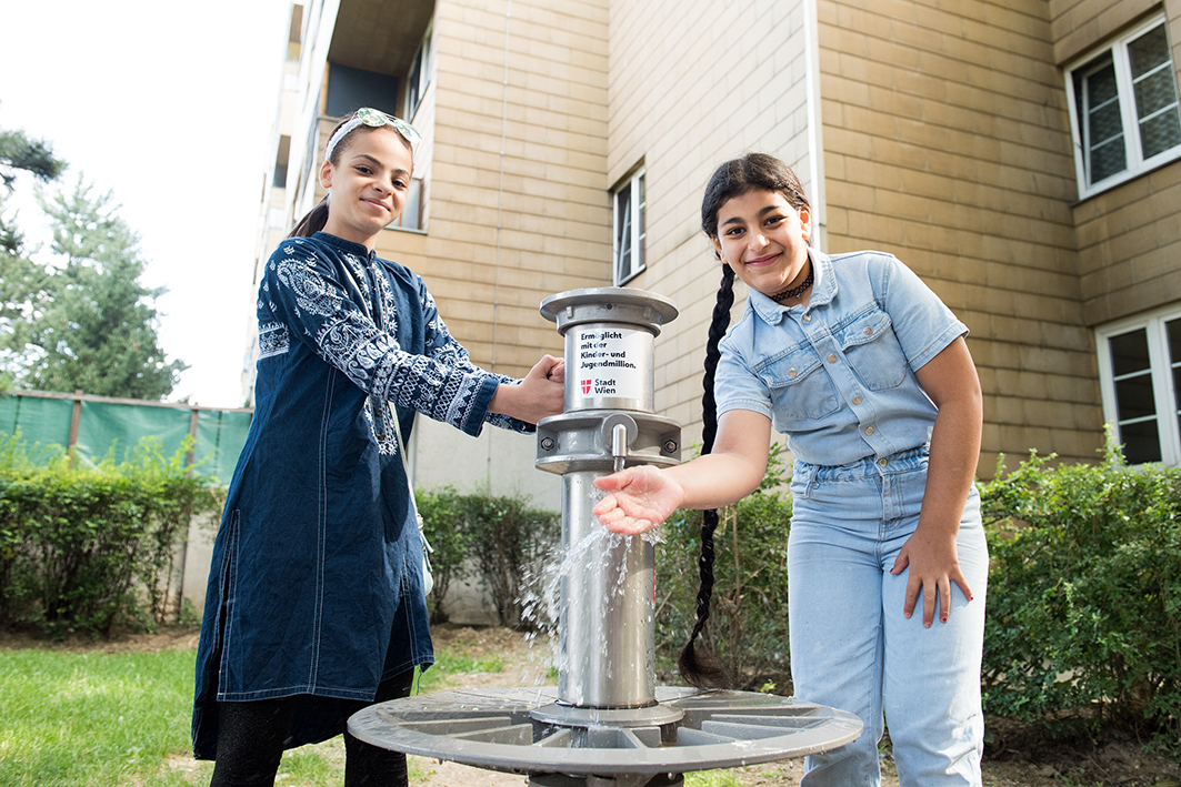 Zwei Mädchen stehen am Wasserbrunnen