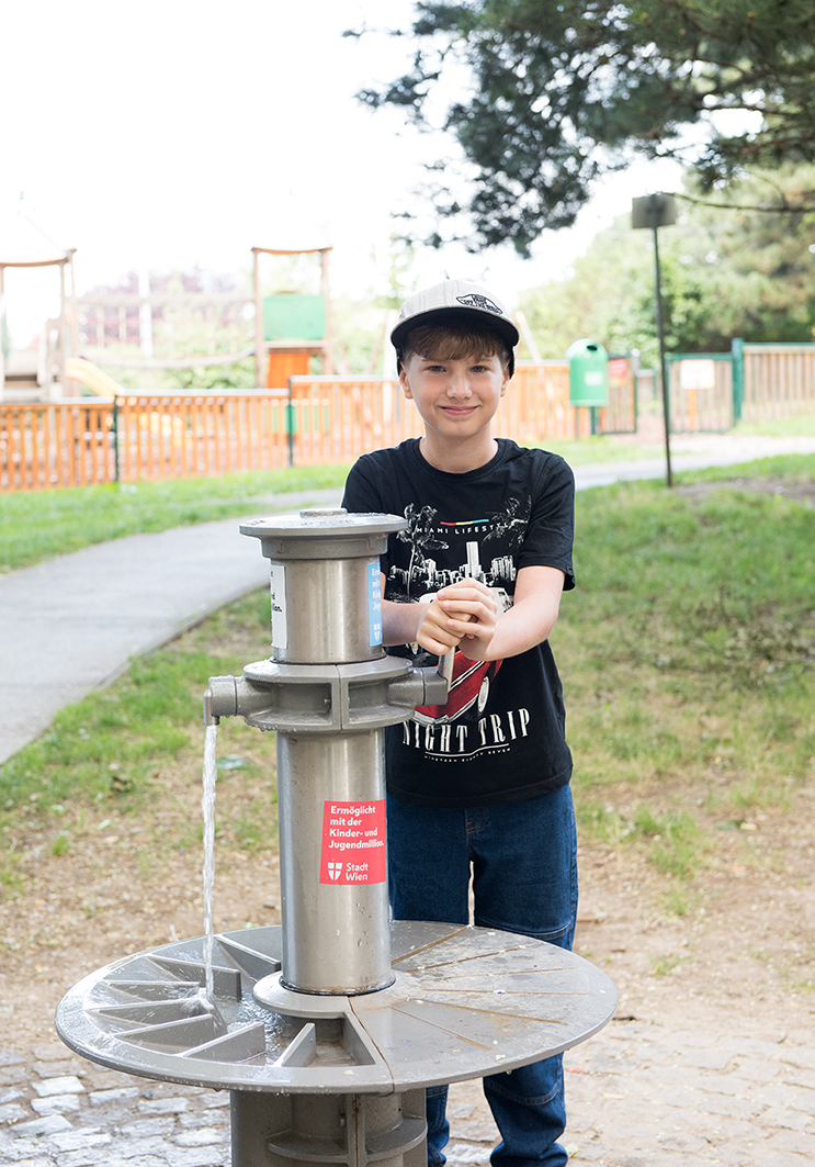 Ein Bub steht am Wasserbrunnen. 